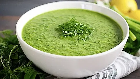 Green detox soup in a white bowl, garnished with fresh herbs